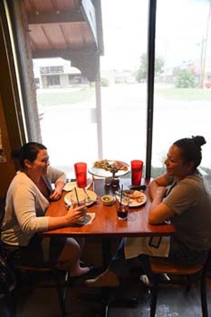 2 women enjoy their pizza by the window watching Western Avenue go by, recently at The Wedge.  mh