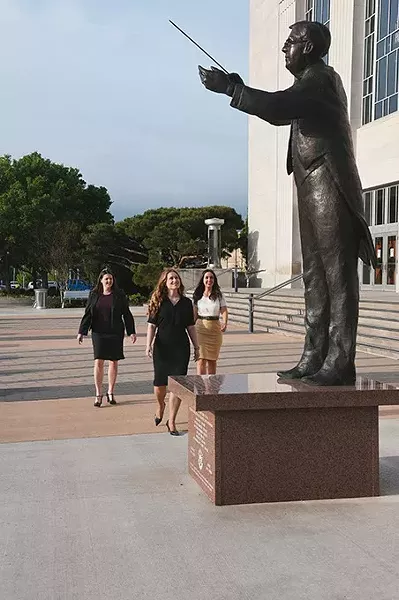 From left, Jenni Fosbenner, Allison Goodman, and Cheryl Brashear, board members with the Overture OKC Philharmonic support group, walk under the conductor sculpture in front of the Civic Center Music Hall in Downtown OKC recently. mh