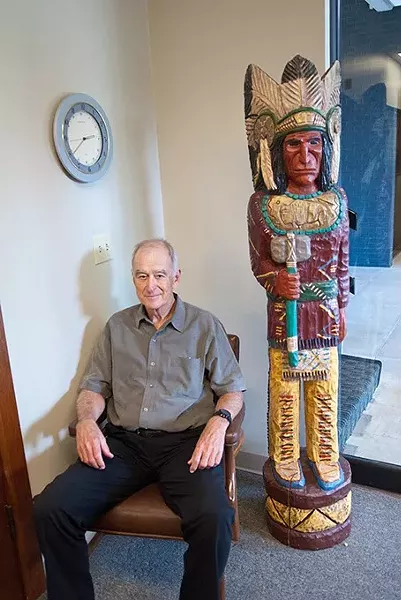 Kent Frates relaxes in the reception area of his office, next to a wooden Indian he collected. He's quite a collector, with eclectic artifacts displayed around his office. mh