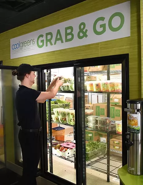 A worker re-stocks the selection of the Grab and Go items at the re-opened downtown CoolGreens. mh
