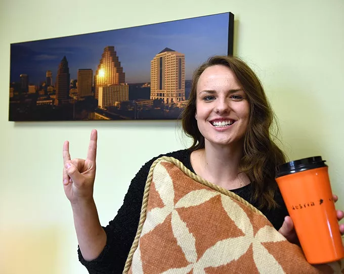 Next to a picture of the Austin skyline while holding a burnt orange pillow and coffee container, Mary Ellen Knewtson gives the "Hook-em-horns" sign, at her office with The Gooden Group in Edmond, 9-29-15. - MARK HANCOCK