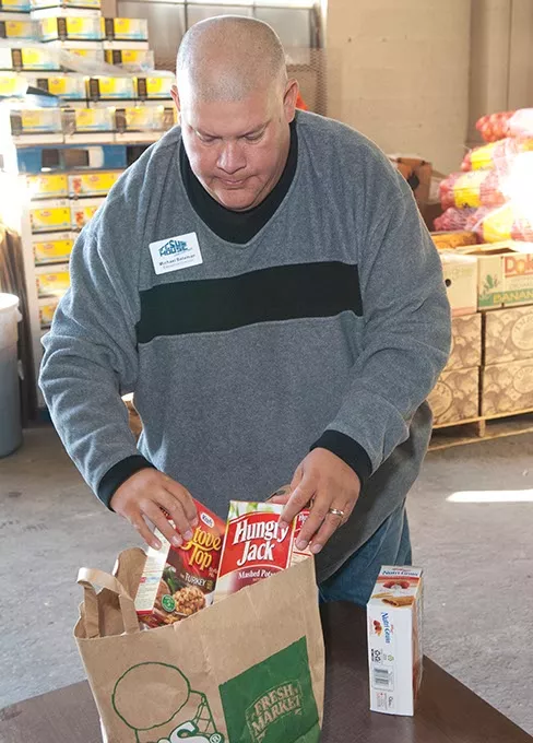 Mike Bateman, executive director at Jesus House, aranges items in a grocery sack, as an example of what will be given to low-income families during this years food basket hand out, in the donations warehouse at Jesus House. mh
