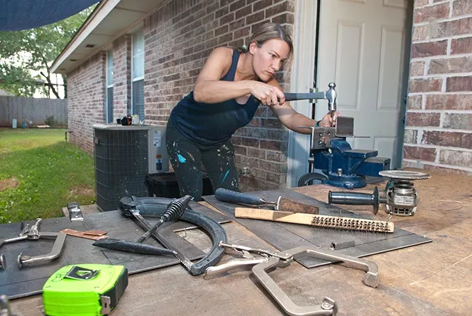 Christie Owen does some finishing touches to her art submission for Refreshing the Palette, a steel sculptured wine bottle holder, in a work area outside her garage in Edmond. mh