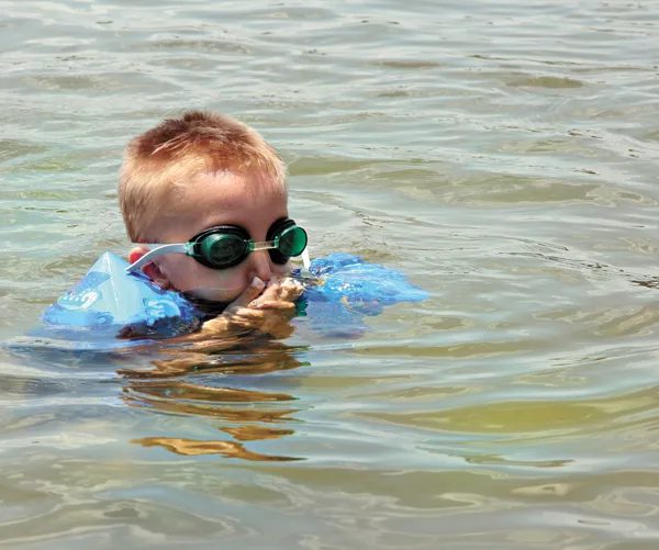 young boy plugs his nose while learning to swim - BIGSTOCK