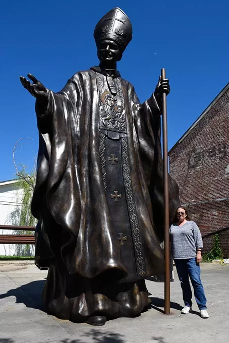 Teresa Clark poses for a photo with a 20-foot-tall monument to Pope John Paul II that she designed, at The Crucible Foundry in Norman, Thursday, May 12, 2016. - GARETT FISBECK