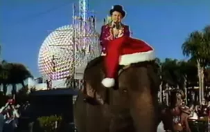 Regis Philbin riding a Santa hatted elephant past a circus in Epcot as part of the 1987 Walt Disney World Christmas Parade television special - IMAGE VIA PROGRESSCITYPUBLICTV | YOUTUBE