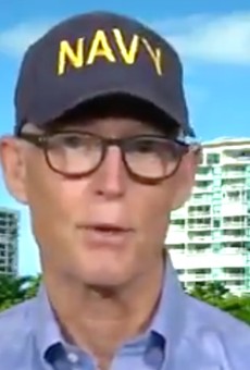 Sen. Rick Scott combines his Navy-hat schtick with his Woody Allen glasses.