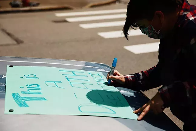 A protester pens a sign to hold during a car-only rally past the Allegheny County Jail in Downtown Pittsburgh. - CP PHOTO: JARED WICKERHAM