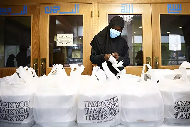 A volunteer puts on gloves before handing out Iftar boxes at the Islamic Center of Pittsburgh during Ramadan on Sun., May 3, 2020. - CP PHOTO: JARED WICKERHAM