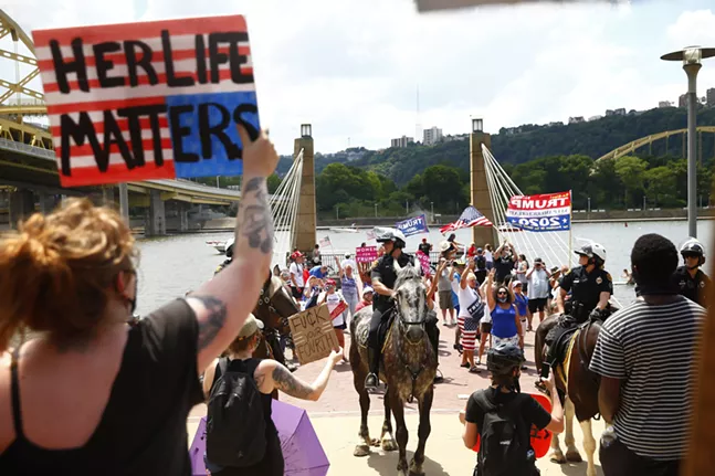 Four mounted Pittsburgh Police officers separate the Anti-Trump protesters from the MAGA boat rally on the North Shore. - CP PHOTO: JARED WICKERHAM