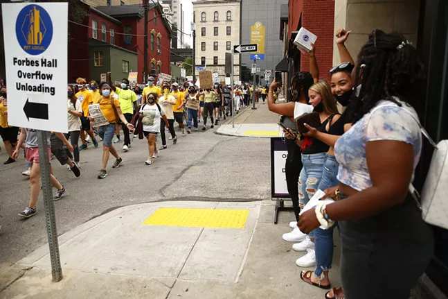 University of Pittsburgh students cheer from in front of Insomnia Cookies as the protest marches through Oakland. - CP PHOTO: JARED WICKERHAM