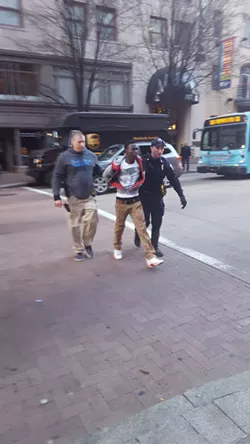 Abdulkadir Abdi being taken across the street from his bus stop on the north side of Liberty Avenue. - PHOTO BY REBECCA NUTTALL