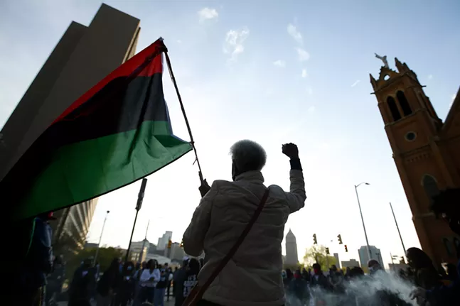 Frankie Harris of the Ujamaa Collective raises a fist and holds up a flag in front of the crowd gathered at Freedom Corner. - CP PHOTO: JARED WICKERHAM