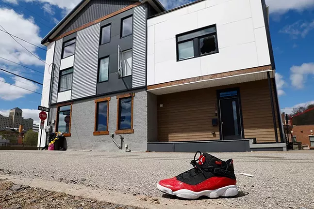 A lone red, black, and white shoe sits on the sidewalk in front of an urban building with shattered windows
