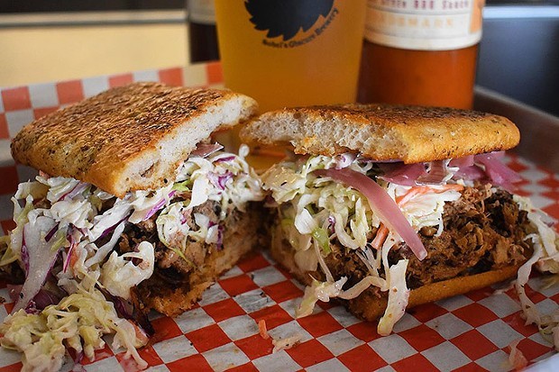 A loaded BBQ sandwich from Spork Pit sits on red and white checkered paper.