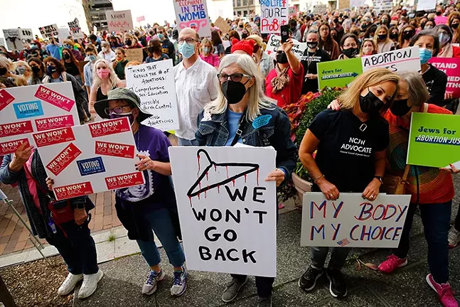 A crowd of people hold up signs for abortion rights, including one in the front that has a picture of a bleeding coat hanger above the words "We won't go back"