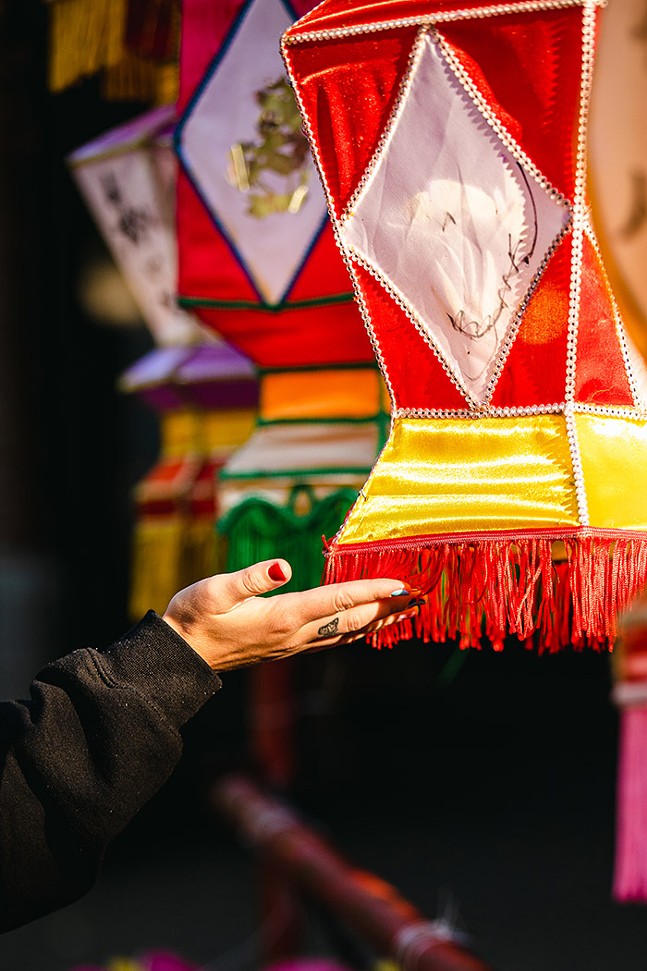 A hand with painted fingernails reaches out to touch the fringe at the bottom of an Asian lantern