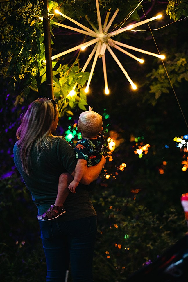 An adult holds a toddler in front of a large star-shaped lantern that looks like fireworks