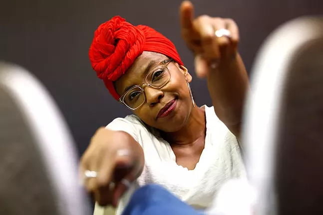 A Black woman points toward the camera.