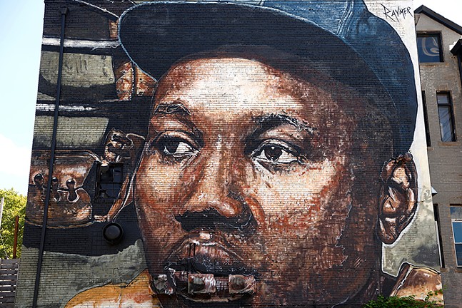 A close-up photograph of a mural of a Black man wearing a baseball hat