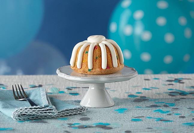 A small bundt cake decorated with white icing sits on a tale decorated for a birthday party.