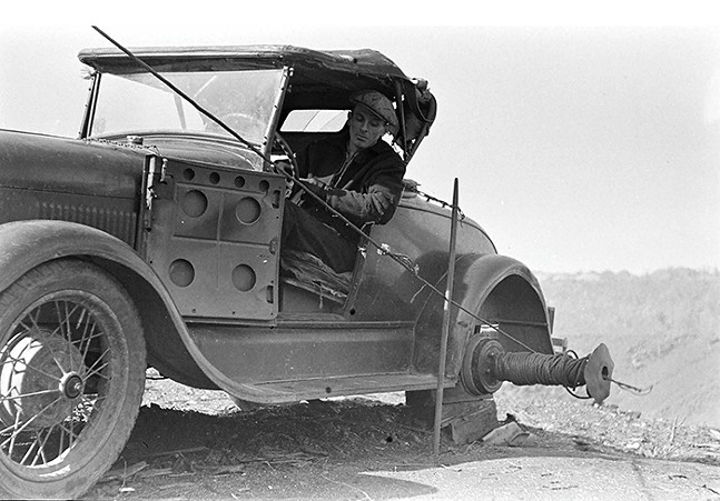 An old black-and-white photo of a man in an old metal car