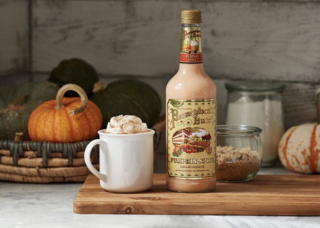 An autumnal kitchen scene surrounds a bottle of Pumpkin Spice Cream Liqueur and a mug topped with whipped cream