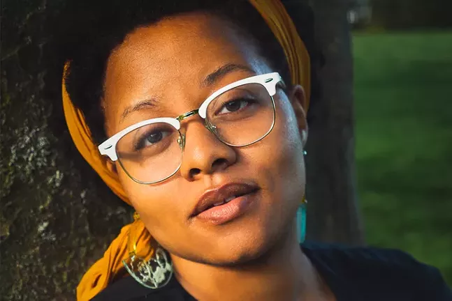 A close-up of Black playwright a.k. payne wearing glasses and a colorful head scarf.