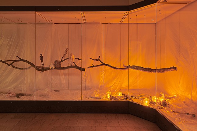 Orange light fills an exhibit area with floating sticks.