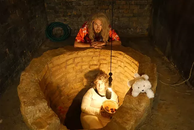 Two people and a stuffed dog surround a replica of the well from the film Silence of the Lambs.