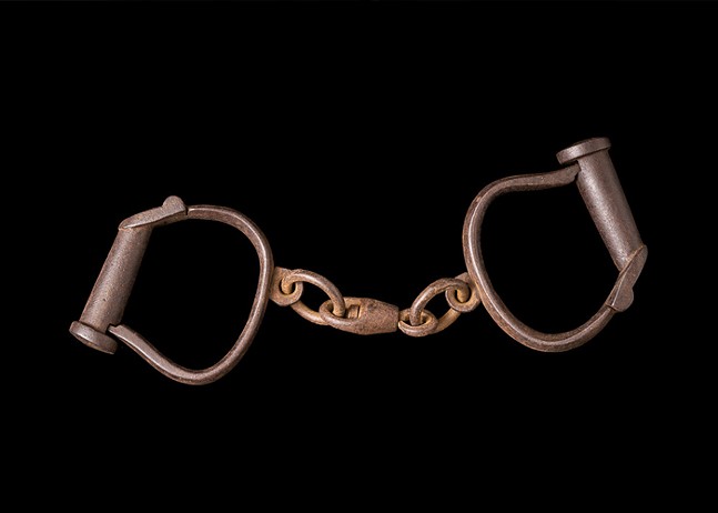 A pair of old, copper-colored handcuffs are presented on a black background.