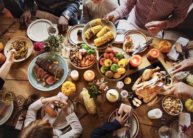 An overhead shot of a table full of a very full Thanksgiving table with people passing dishes.