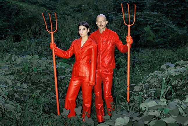 The rock duo Mattial stands in a green, leafy space dressed in devil costumes and holding red pitchforks.