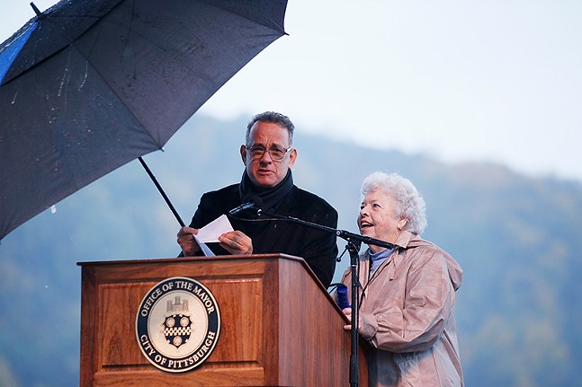 Actor Tom Hanks and Joanne Rogers stand at a podium under an umbrella during a rally in Downtown Pittsburgh.