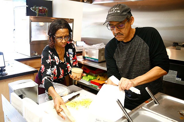A Black man and woman pack up food in the kitchen of a restaurant.
