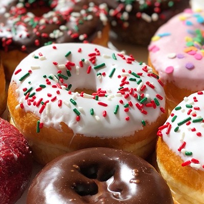 An assortment of brightly colored donuts cover in various icings, including rainbow-colored sprinkles on white icing, chocolate icing, and pink icing
