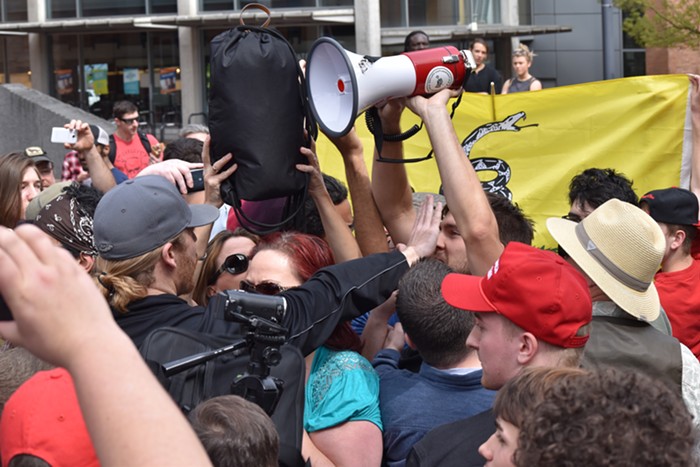 An Infowars guy puts his hand in the face of an anti-Trump guy, who used the siren from his megaphone for most of the rally