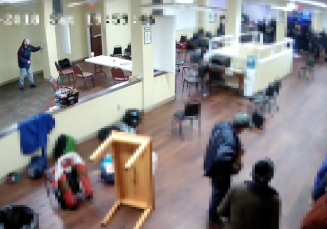 Elifritz stands in the top left corner of this video capture—hiding from police behind a pillar.