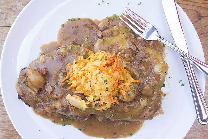 The pork schnitzel is smothered in beer bacon bratwurst gravy and melted gruyere, then topped with carrot kraut slaw. - PHOTO BY MABEL SUEN