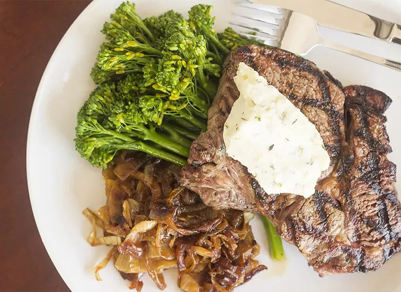 The hand-cut beef ribeye features a twelve-ounce portion served with bleu-cheese butter, whiskey onions and a vegetable side. - MABEL SUEN