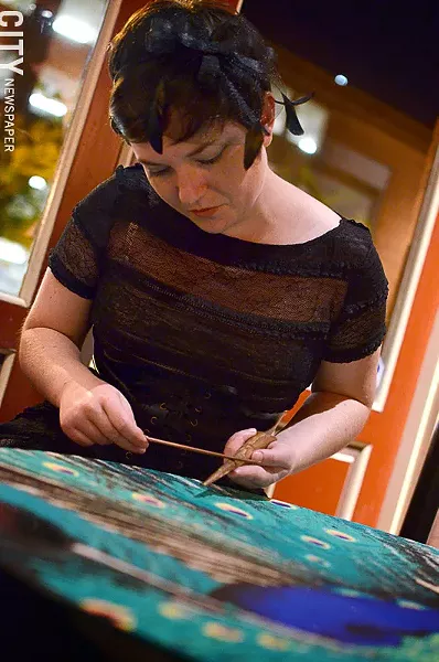 Artist Katie Jo Suddab works on a peacock sand mandala in Geva’s cafe. - PHOTO BY MATT DETURCK