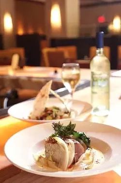 From front: Prosciutto-wrapped Chilean sea bass on an endive fondue with fried spinach and toasted garlic; grilled romaine and radicchio chopped salad with roasted romas, cannellini beans, ricotta salata, and sherry vinaigrette topped with Lavash flat bread; a bottle and glass of a 50-50 blend of chardonnay and pinot grigio by Le Rime.