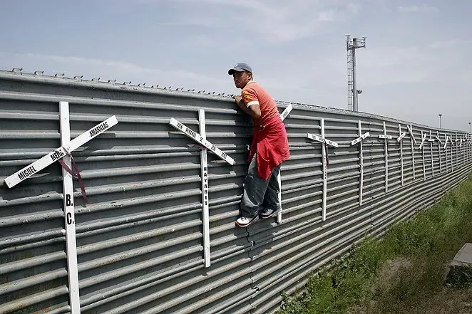 An aspiring migrant scales a fence to cross the U.S.-Mexico border. - WIKIMEDIA COMMONS