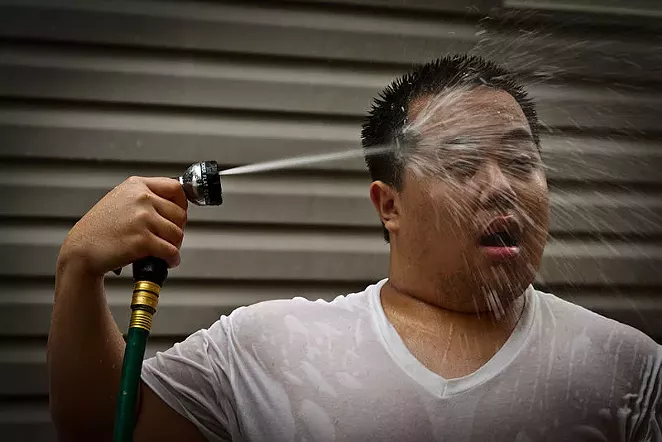 A man seeks relief from the heat by blasting himself in the face with a garden hose. - INSTANT VINTAGE