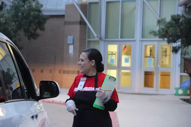 A cafeteria worker with Schertz-Cibolo-Universal City ISD helps with curbside meal pickup. - WE GO PUBLIC