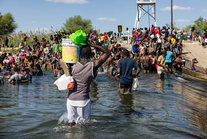 Migrants crossed the Rio Grande between Texas and Mexico with supplies Thursday as they prepared to spend the night under the international bridge connecting Del Rio and Ciudad Acuña. - TEXAS TRIBUNE / JORDAN VONDERHAAR