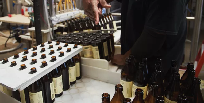 14. Giles moves newly labeled bottles to be filled and capped.