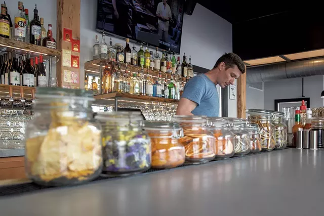 Bartender Woody Wright-Moore standing behind jars of housemade dried fruits used for custom cocktails - JAMES BUCK