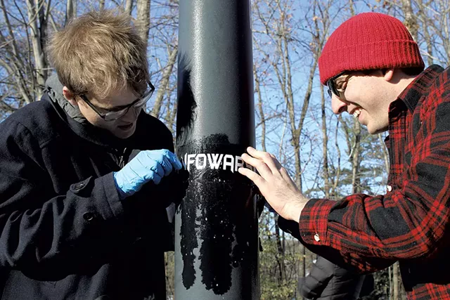 Kason Hudman (left) and Walter Keady trying to remove an Infowars sticker on Riverside Avenue - COURTNEY LAMDIN