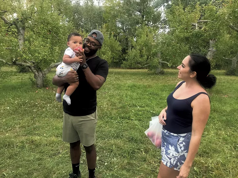 Luka McKenzie eating his first apple at Shelburne Orchards, with parents Junior McKenzie and Sheena Barcomb - SALLY POLLAK ©️ SEVEN DAYS